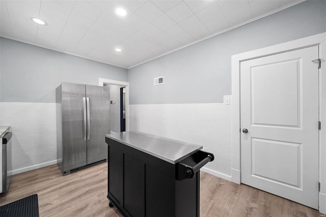 kitchen with light wood-type flooring, wainscoting, dark cabinets, and freestanding refrigerator