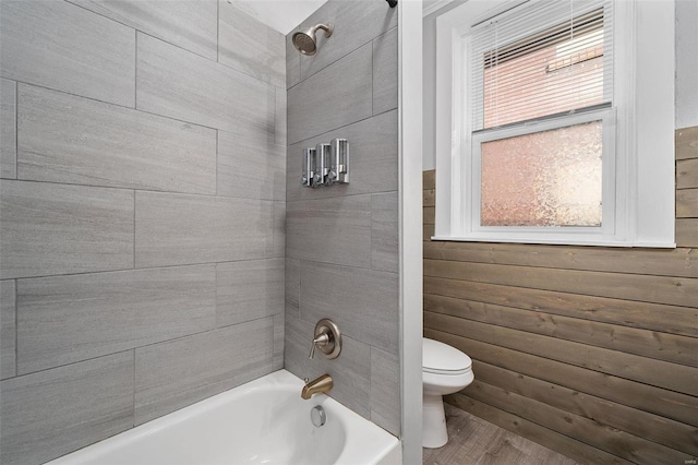 full bath with shower / bath combination, wood walls, toilet, and wood finished floors