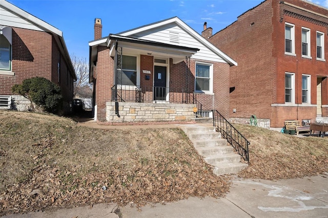 view of front of home featuring covered porch, a chimney, and brick siding