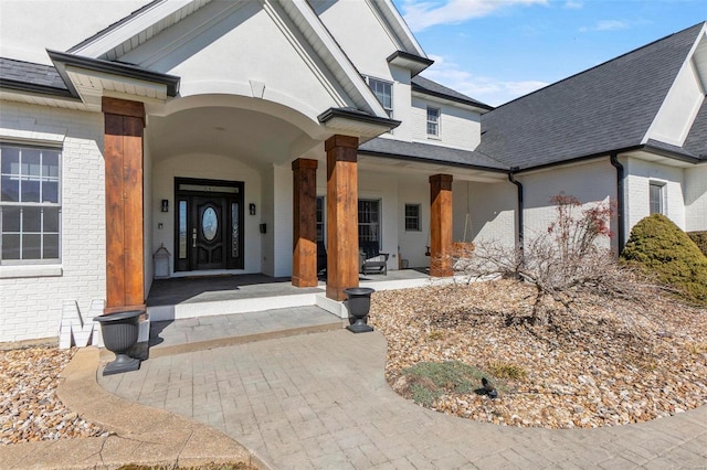 view of exterior entry featuring brick siding and roof with shingles