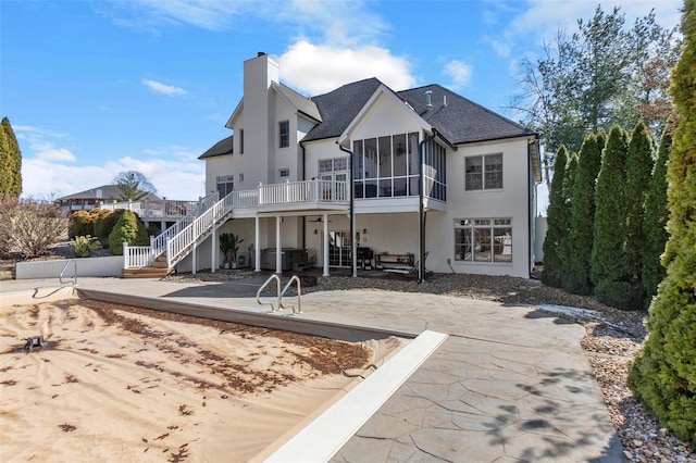 back of house with a chimney, stucco siding, stairway, a sunroom, and a patio area