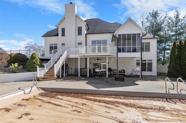 back of house featuring a patio, a sunroom, a chimney, stairway, and stucco siding