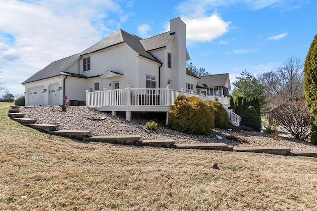 back of property featuring a garage, covered porch, a chimney, and a lawn