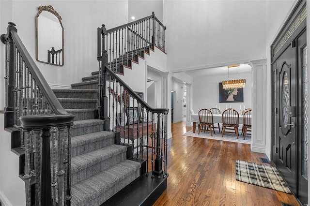 entrance foyer featuring baseboards, wood finished floors, a towering ceiling, and ornate columns