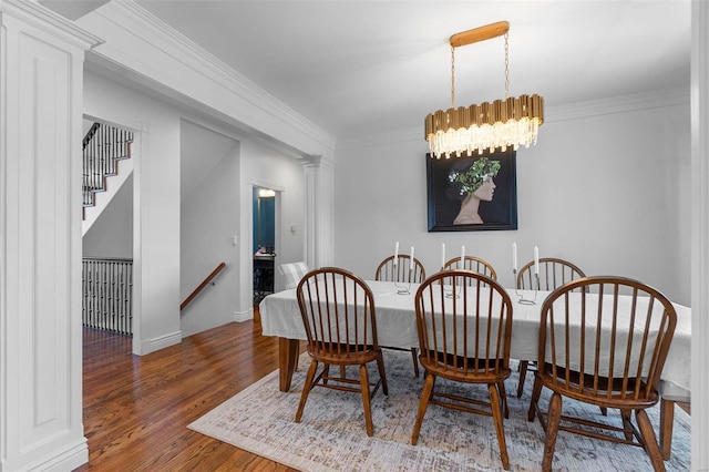 dining area featuring a notable chandelier, crown molding, wood finished floors, and ornate columns