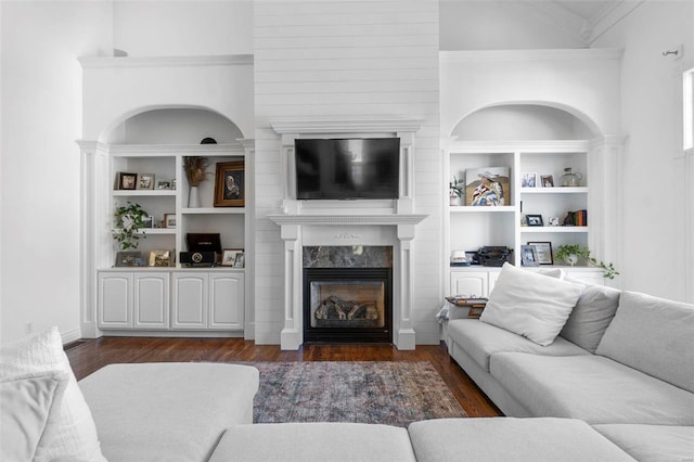 living room featuring built in features, wood finished floors, crown molding, and a premium fireplace