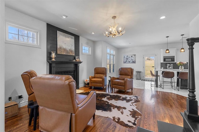 living room with a chandelier, a glass covered fireplace, a healthy amount of sunlight, and wood finished floors