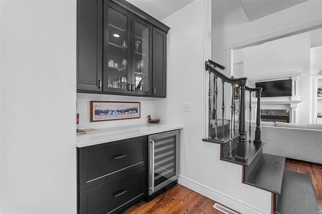 bar featuring a dry bar, beverage cooler, dark wood finished floors, stairway, and a high end fireplace