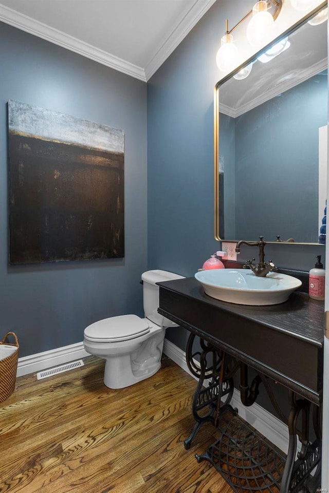 half bathroom with wood finished floors, a sink, baseboards, visible vents, and crown molding