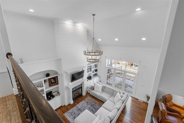 living area with a chandelier, recessed lighting, wood finished floors, a glass covered fireplace, and crown molding