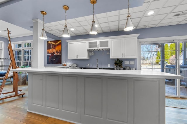 kitchen with glass insert cabinets, light countertops, light wood-type flooring, white cabinetry, and pendant lighting