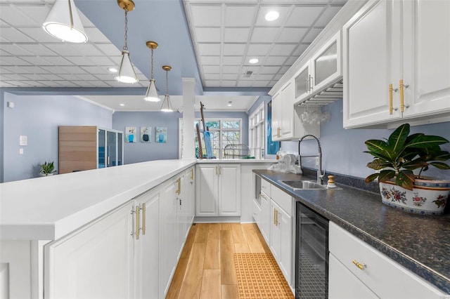 kitchen with light wood-style flooring, beverage cooler, a sink, white cabinets, and decorative light fixtures