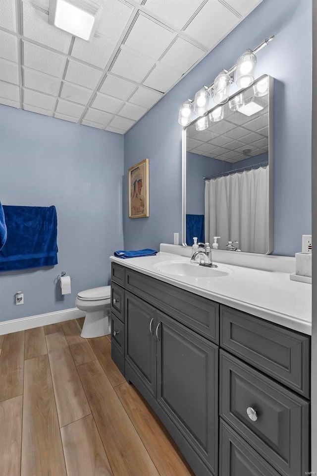 full bath featuring toilet, a paneled ceiling, wood finished floors, vanity, and baseboards