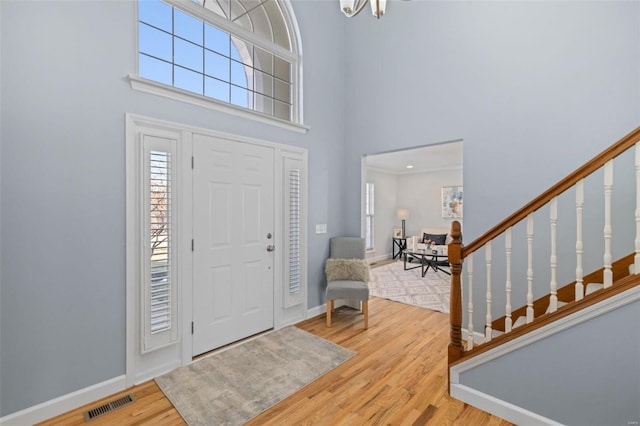 foyer featuring a high ceiling, stairs, visible vents, and wood finished floors