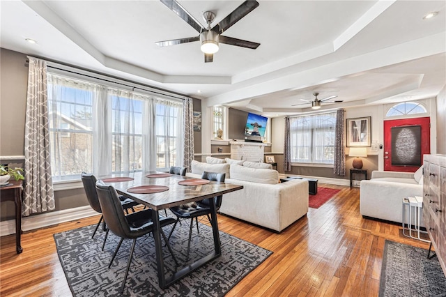 dining room featuring ceiling fan, baseboards, a raised ceiling, and light wood-style floors