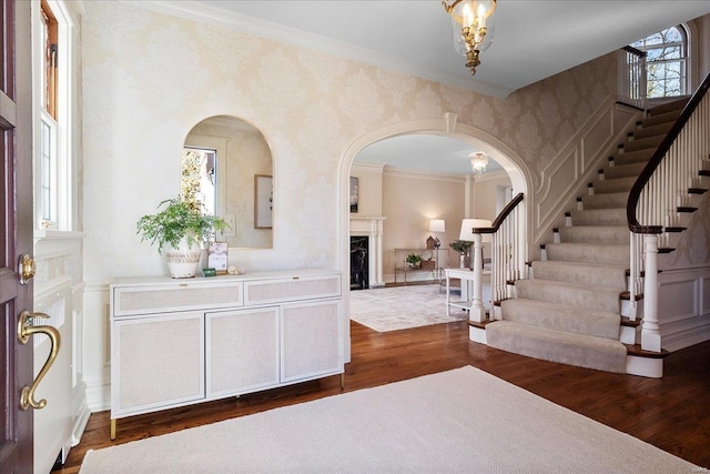 entryway with dark wood-style flooring, a fireplace, crown molding, and stairs