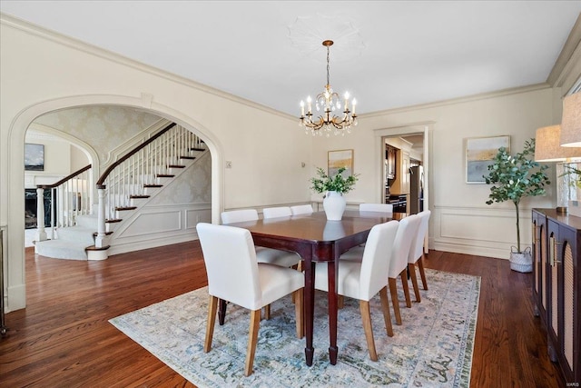 dining area featuring arched walkways, dark wood-style flooring, stairs, and a decorative wall