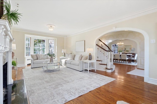 living area with arched walkways, a notable chandelier, a fireplace, wood finished floors, and ornamental molding