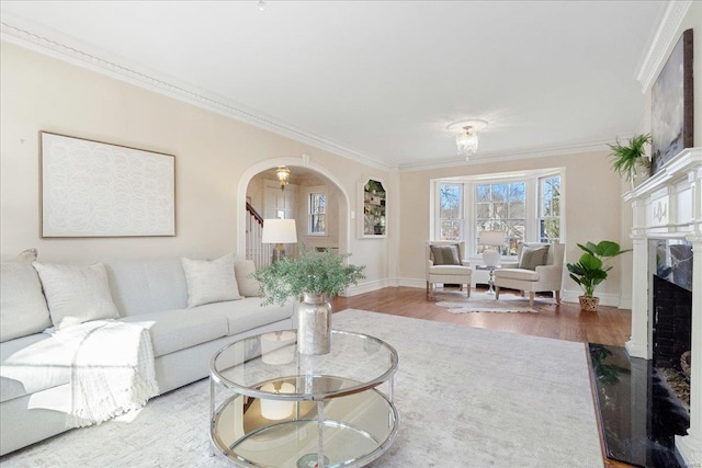 living area featuring arched walkways, wood finished floors, a high end fireplace, stairs, and crown molding