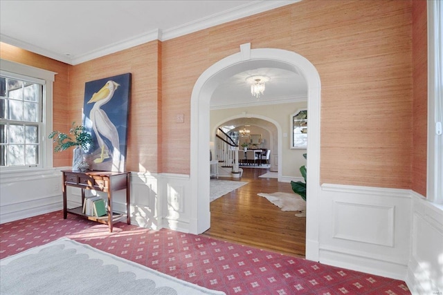 foyer featuring arched walkways, a wainscoted wall, crown molding, a notable chandelier, and stairway