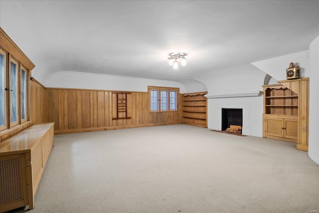 living room featuring a fireplace with flush hearth, wooden walls, vaulted ceiling, and carpet flooring