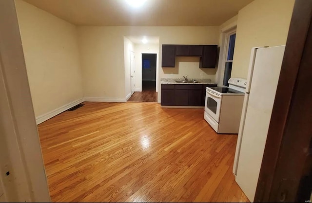 kitchen featuring light countertops, light wood-style floors, a sink, white appliances, and baseboards