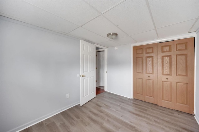 unfurnished bedroom featuring a closet, a drop ceiling, baseboards, and wood finished floors