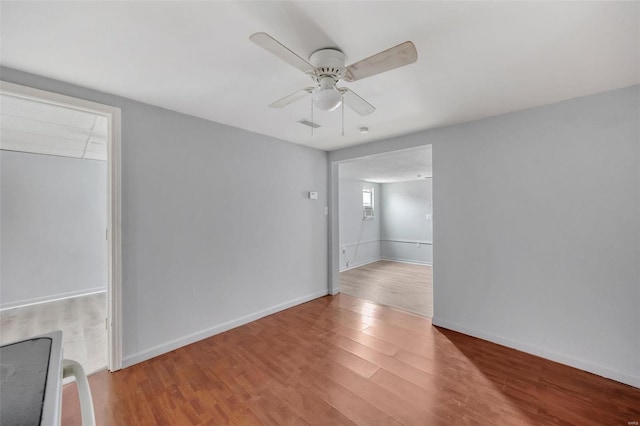 empty room featuring a ceiling fan, visible vents, baseboards, and wood finished floors