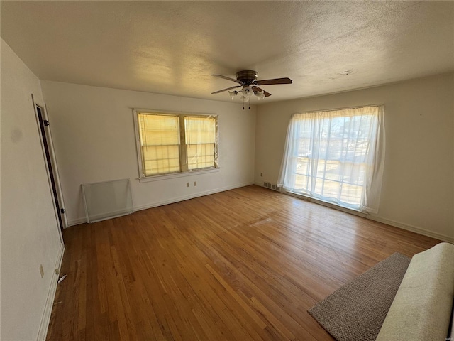 unfurnished room with baseboards, visible vents, a ceiling fan, wood finished floors, and a textured ceiling