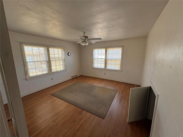 spare room featuring a textured ceiling, wood finished floors, visible vents, and baseboards