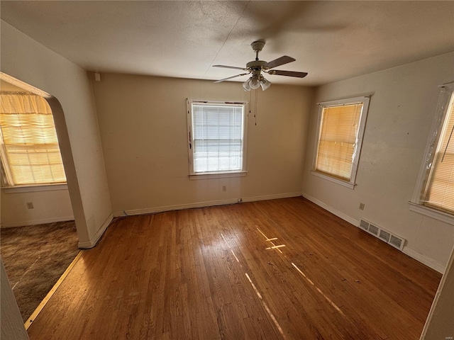 empty room with baseboards, visible vents, arched walkways, and dark wood-style flooring