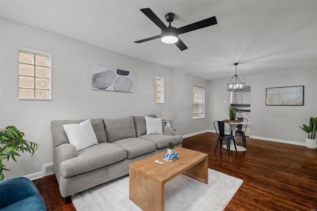 living area featuring ceiling fan with notable chandelier, visible vents, baseboards, and wood finished floors