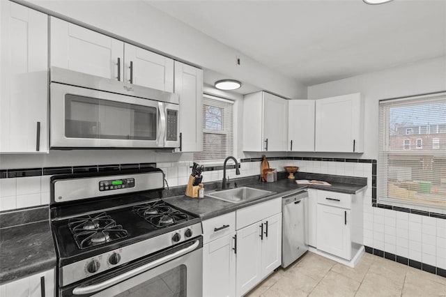 kitchen featuring white cabinets, dark countertops, appliances with stainless steel finishes, a sink, and light tile patterned flooring