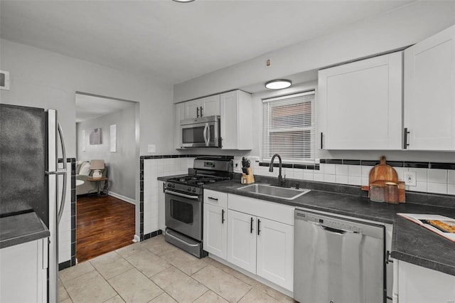 kitchen with light tile patterned floors, dark countertops, appliances with stainless steel finishes, white cabinetry, and a sink