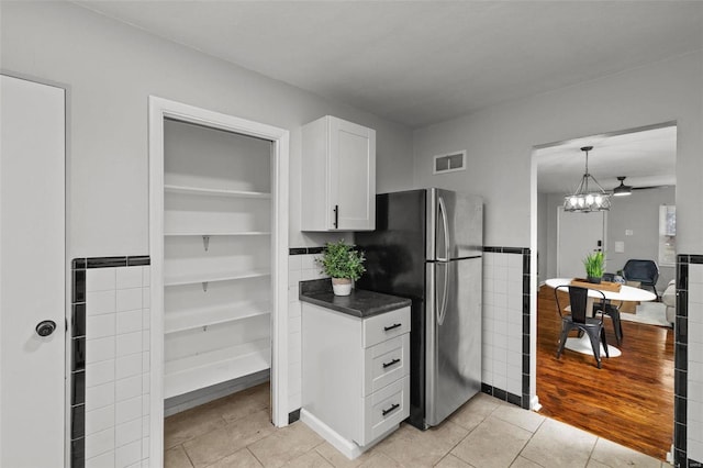 kitchen featuring visible vents, white cabinets, dark countertops, freestanding refrigerator, and light tile patterned flooring