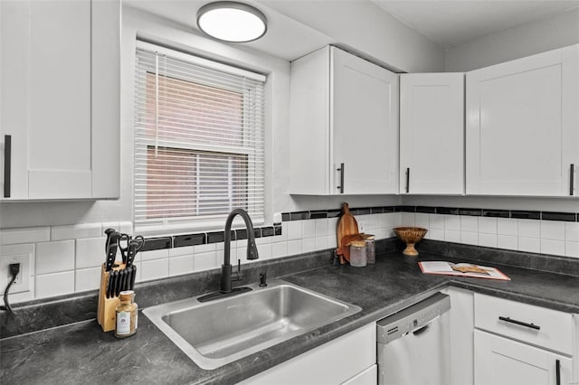 kitchen featuring dark countertops, backsplash, stainless steel dishwasher, white cabinets, and a sink