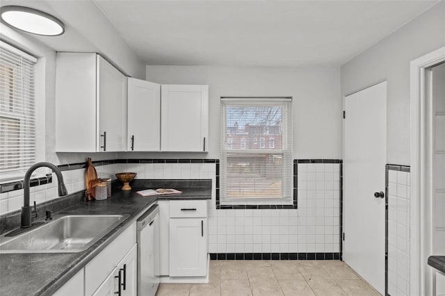 kitchen featuring dark countertops, light tile patterned flooring, a sink, and stainless steel dishwasher