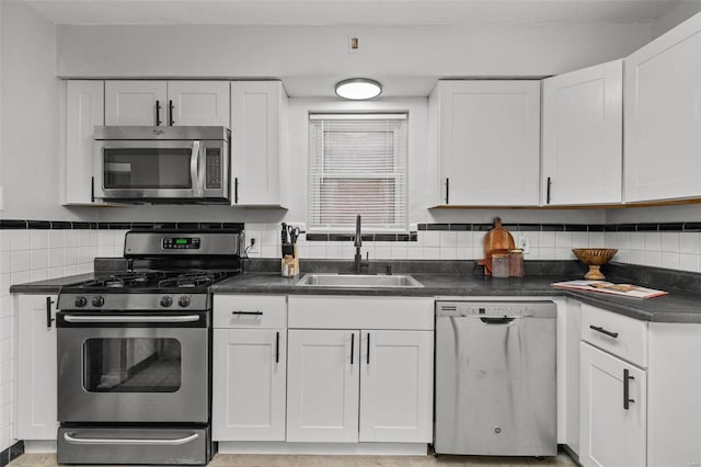 kitchen with appliances with stainless steel finishes, dark countertops, a sink, and white cabinets