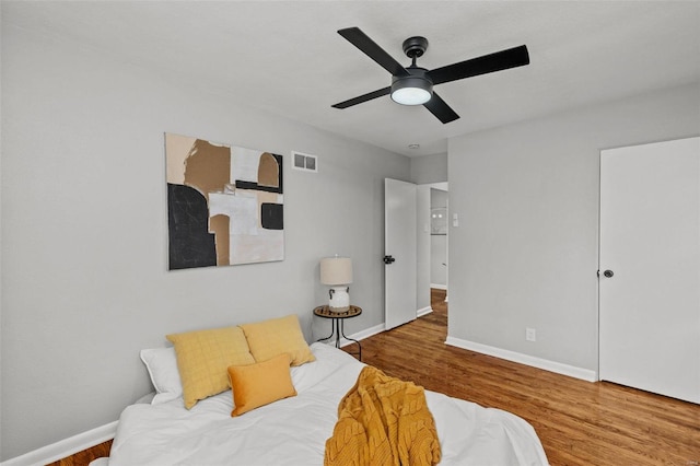 bedroom with a ceiling fan, wood finished floors, visible vents, and baseboards