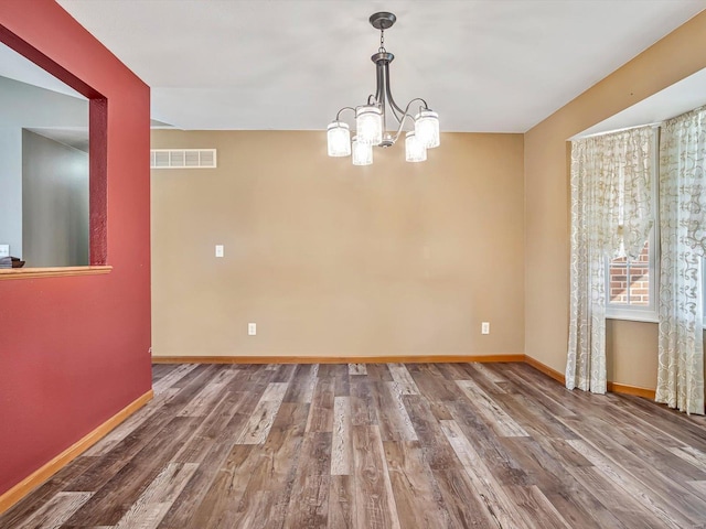 unfurnished dining area featuring a chandelier, wood finished floors, visible vents, and baseboards