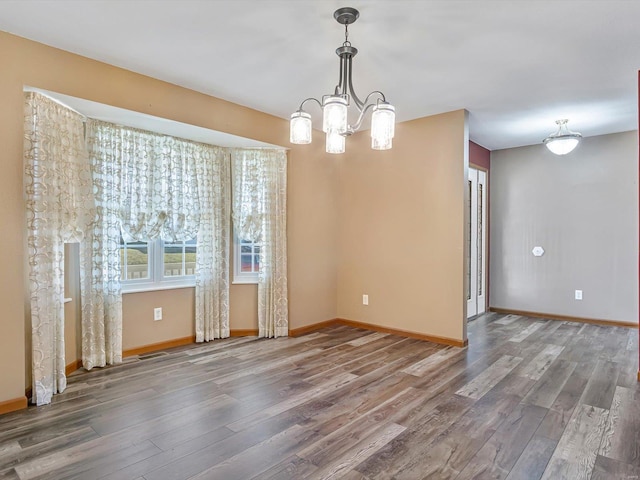 unfurnished dining area featuring an inviting chandelier, wood finished floors, and baseboards