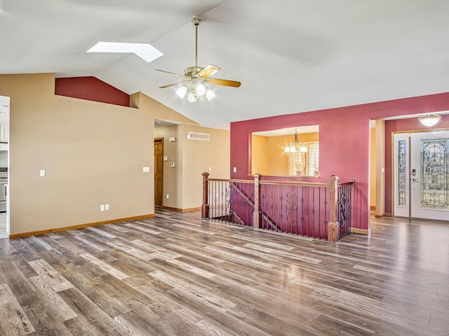 interior space with vaulted ceiling with skylight, baseboards, visible vents, wood finished floors, and ceiling fan with notable chandelier