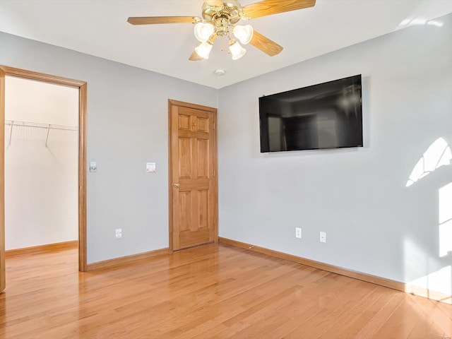 unfurnished bedroom with light wood finished floors, baseboards, ceiling fan, a walk in closet, and a closet