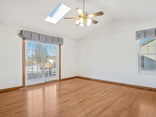 spare room featuring lofted ceiling with skylight, light wood-style flooring, baseboards, and ceiling fan