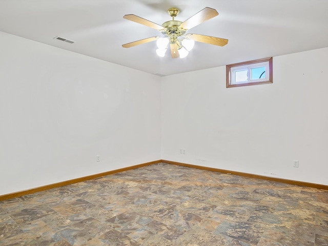 empty room with stone finish flooring, visible vents, ceiling fan, and baseboards