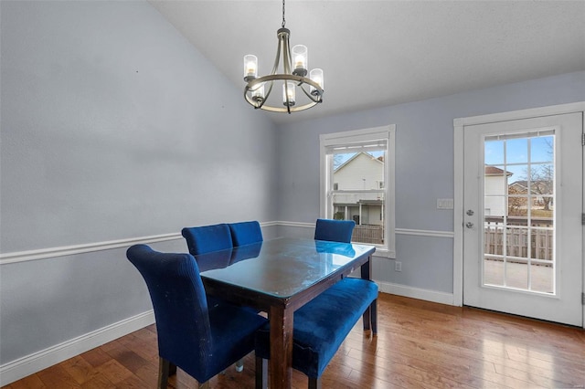 dining space featuring hardwood / wood-style floors, baseboards, a chandelier, and vaulted ceiling