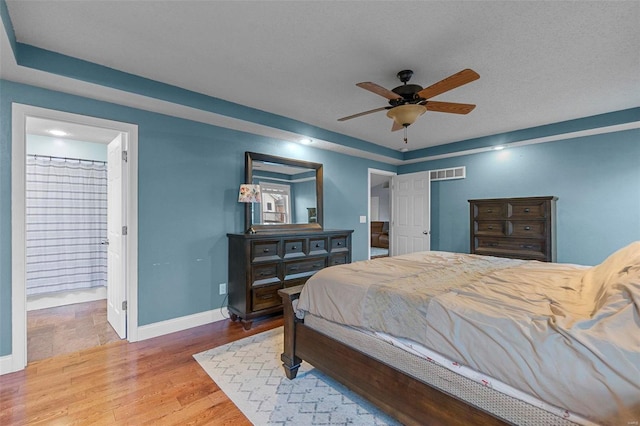 bedroom with wood finished floors, visible vents, baseboards, ensuite bath, and ceiling fan