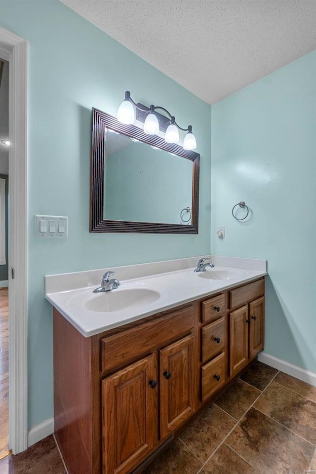 full bath with a textured ceiling, double vanity, baseboards, and a sink