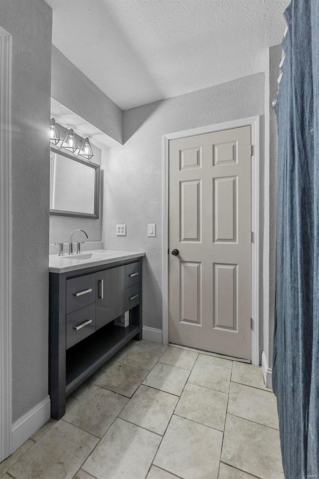 bathroom with tile patterned flooring, baseboards, vanity, and a textured wall