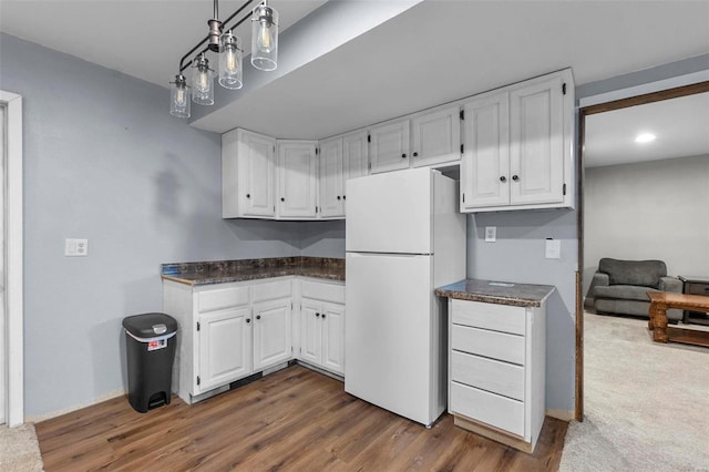 kitchen with dark countertops, wood finished floors, white cabinetry, freestanding refrigerator, and baseboards